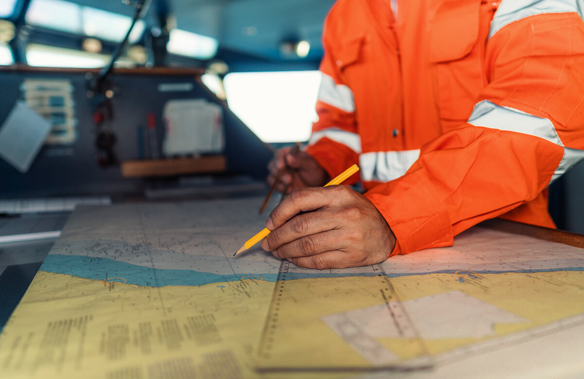 A deck officer on bridge of vessel wearing coverall during navigaton watch at sea . He is plotting position on chart