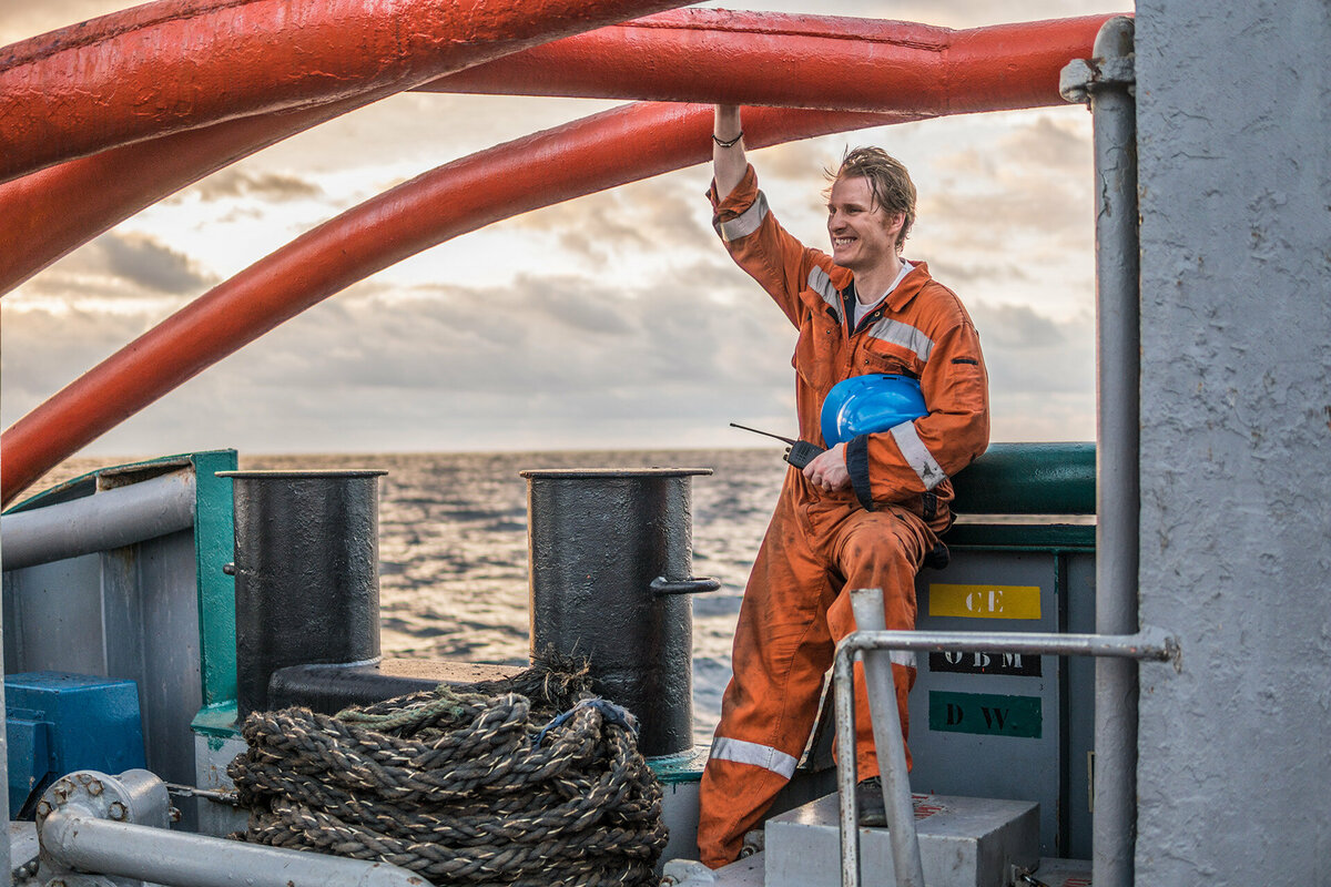 Chief mate on deck of offshore vessel, wearing PPE personal protective equipment - helmet, coverall. He is smiling